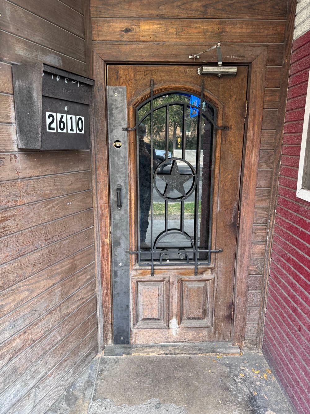 Wooden front door with metal star design and mailbox labeled 2610, set in rustic wall.