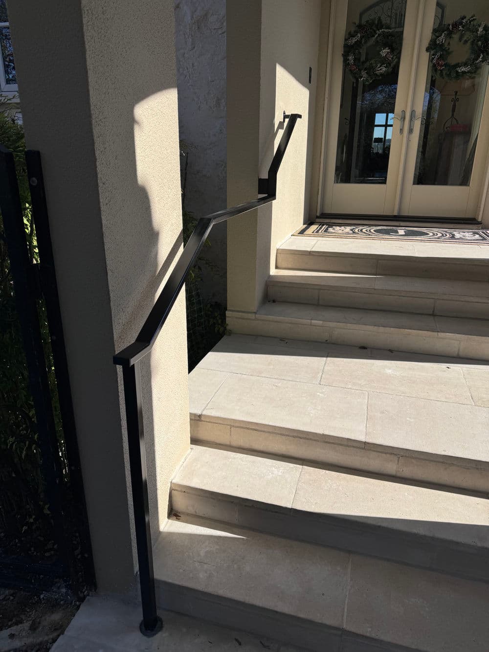 Black handrail on exterior steps leading to a double door entrance, providing support.