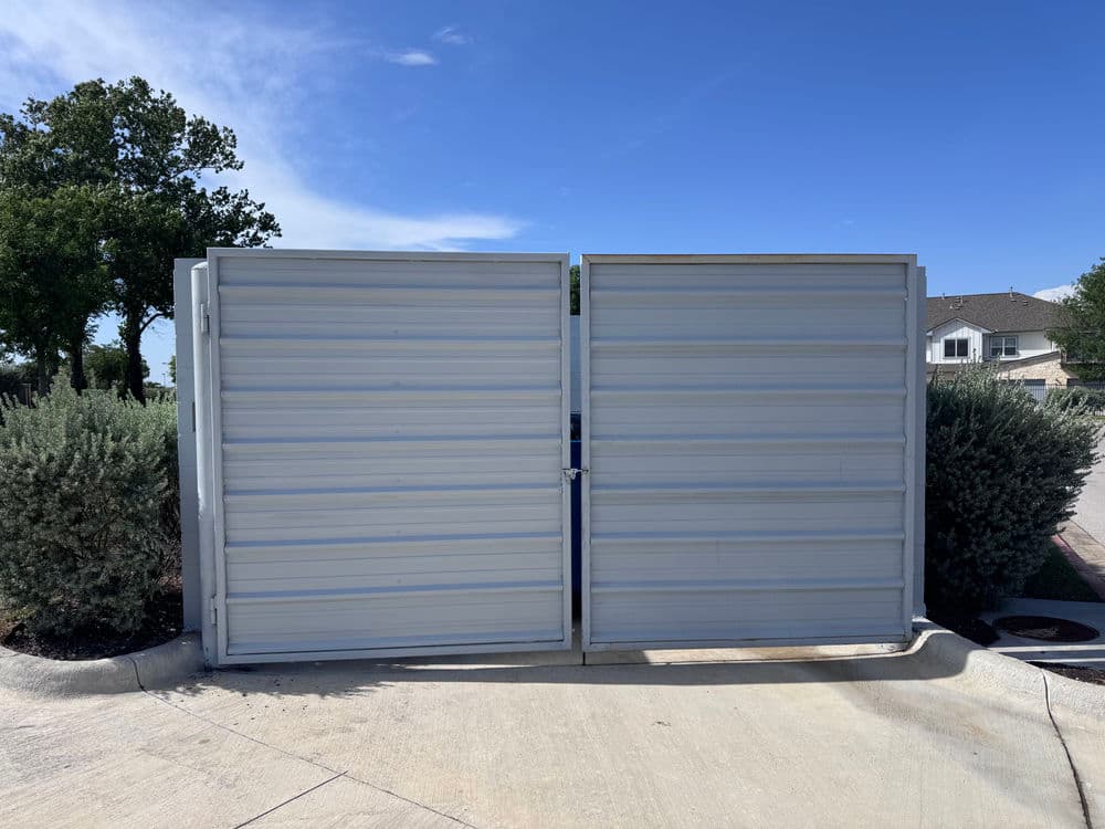 Metal privacy gate in a residential area, surrounded by shrubs and clear blue sky.