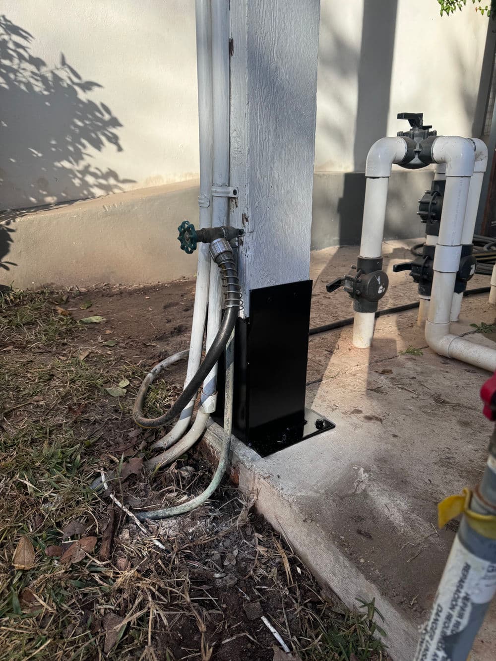 Pipes and faucet installation at building foundation with grass and soil background.