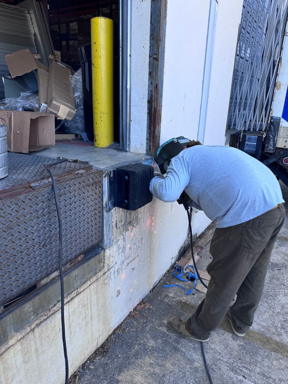 Welder working on steel at loading dock, sparks flying in industrial setting.