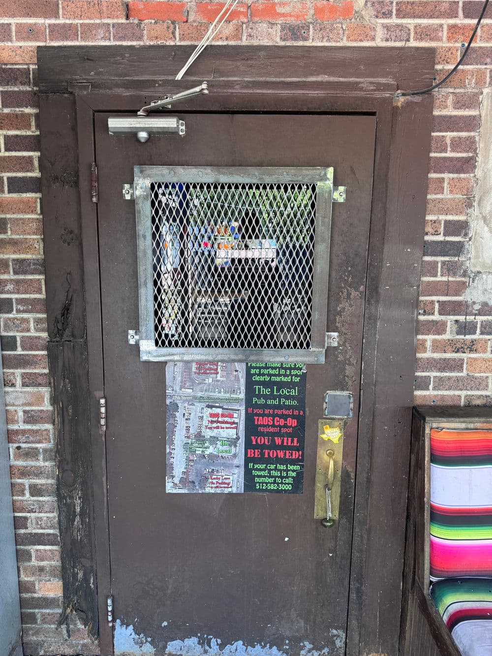 Metal door with mesh screen, marked with local pub signage and towing notice.