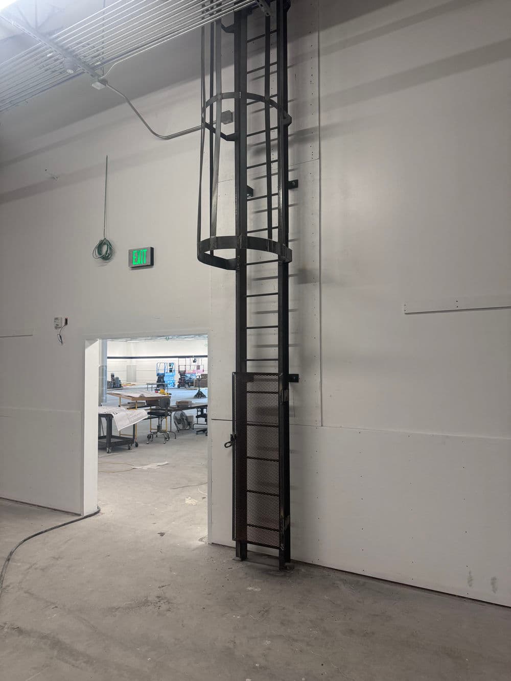 Industrial spiral ladder against a white wall in a warehouse setting.