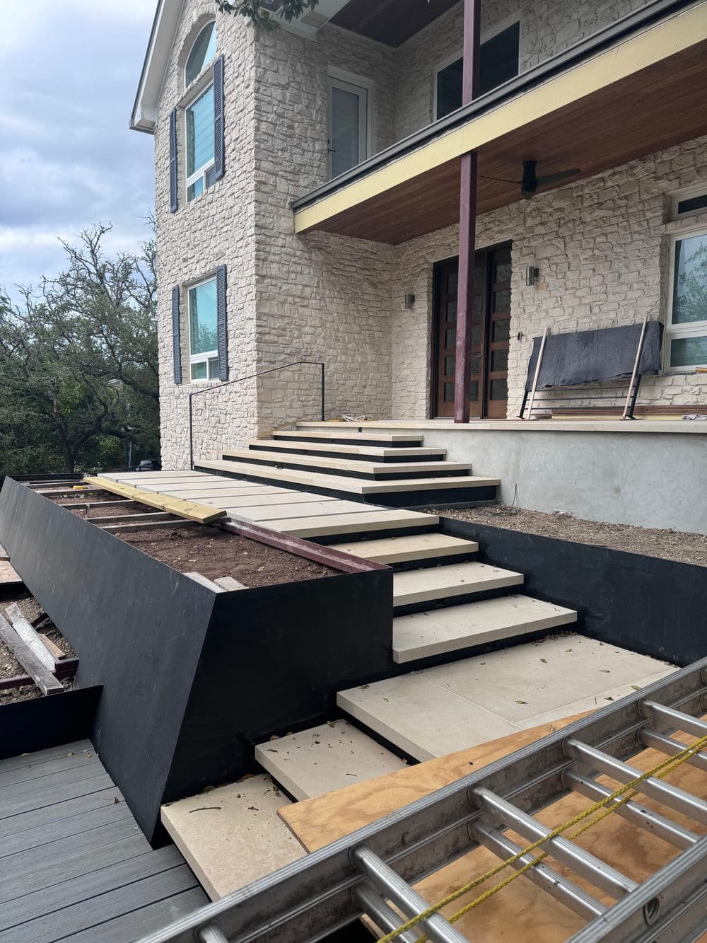 Modern exterior steps under construction with stone house and wooden deck.