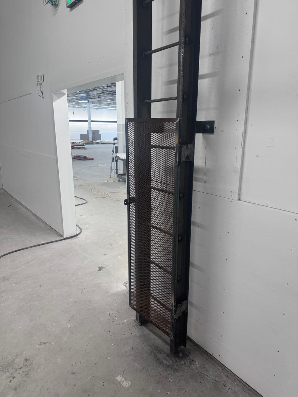 Metal ladder with safety gate in an industrial setting, featuring a textured surface.