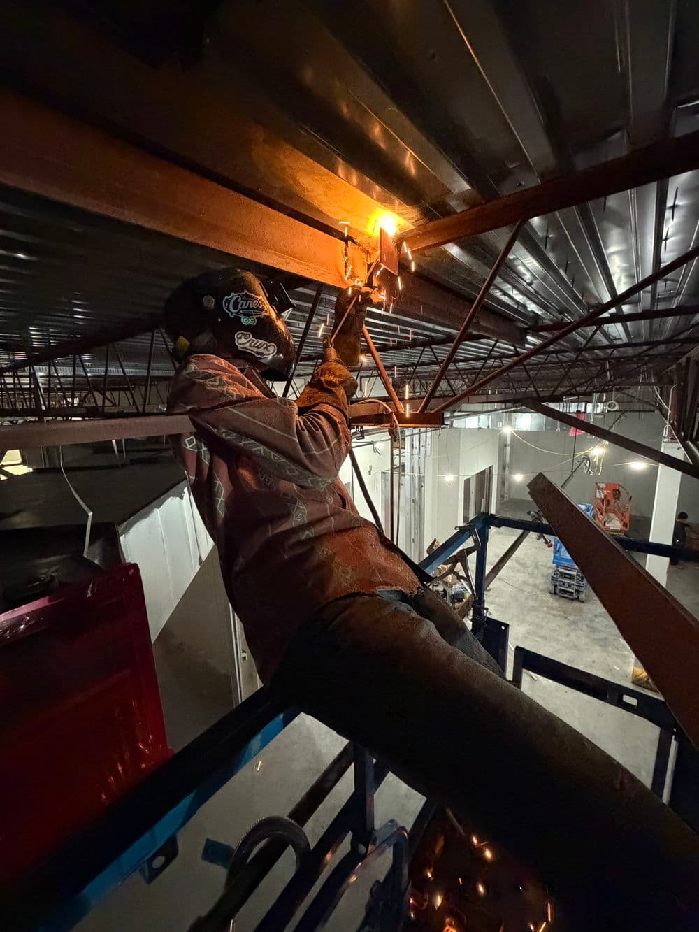 Welder working on metal beams inside a construction site, using a torch for welding.