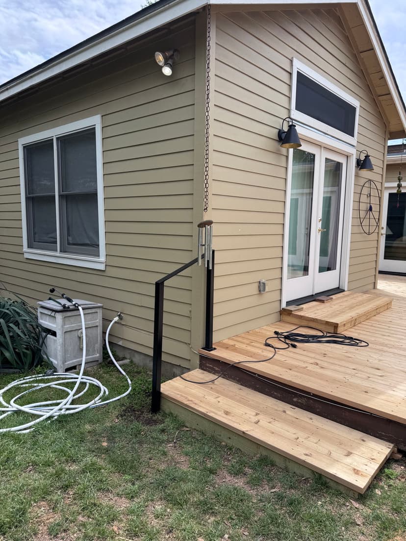 Exterior view of a house with a wooden deck, railing, and garden hose nearby.