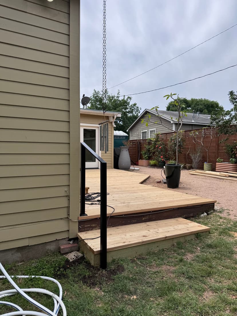 Wooden deck with railing, garden area, and plants near a beige house exterior.