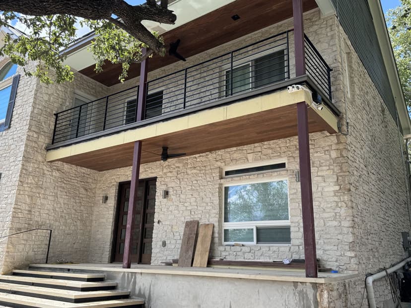 Modern two-story home with a stone facade and a wooden balcony. Clear view of entrance and landscaping.